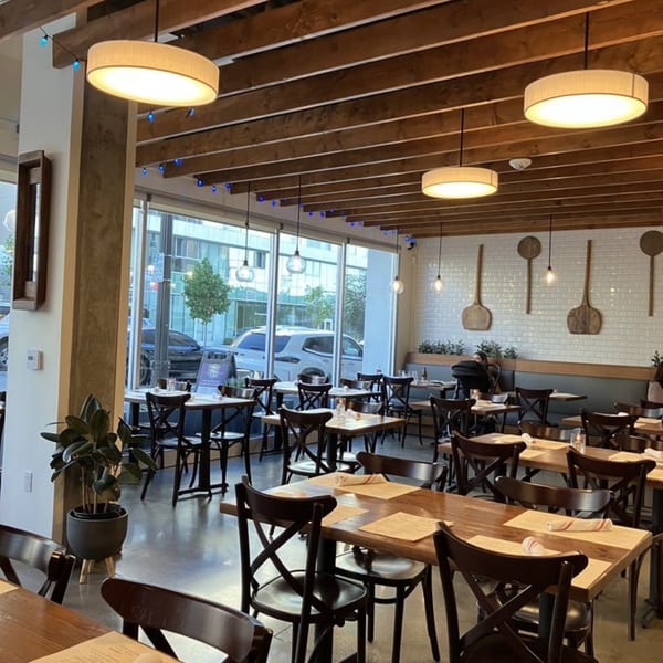 Interior of La Bella Pinseria Romana, showing dining tables, chairs, and large windows.