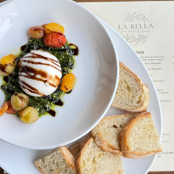 La Bella Pinseria Romana's burrata with pesto, roasted tomatoes, and balsamic glaze, served with bread.