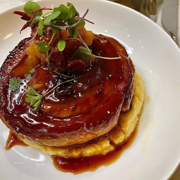 Braised pork cheek with polenta, garnished with microgreens and a rich brown sauce.
