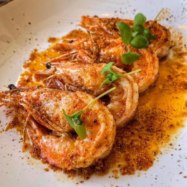 Four large, seasoned shrimp in a rich, orange sauce, garnished with fresh green herbs on a white plate.