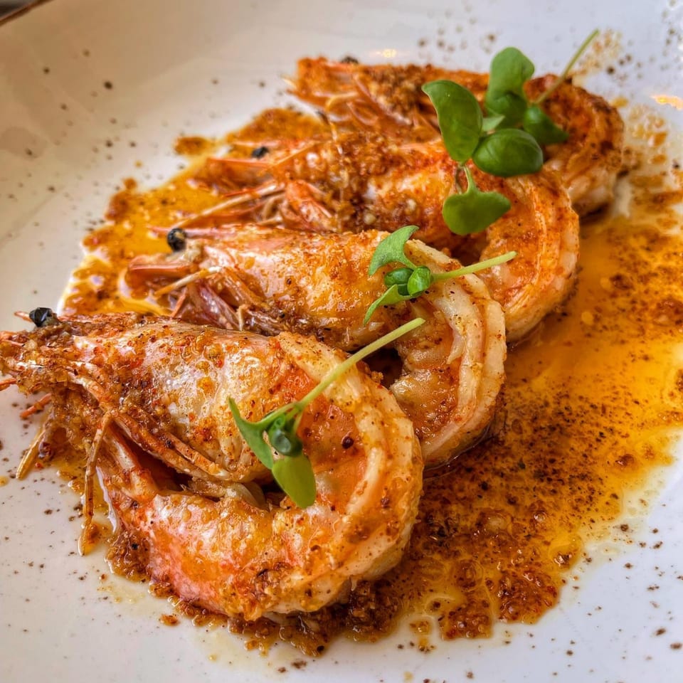 Four large, seasoned shrimp in a rich, orange sauce, garnished with fresh green herbs on a white plate.