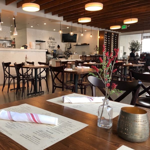 Interior of La Bella Pinseria Romana, showing dining tables, a bar area, and wine racks.