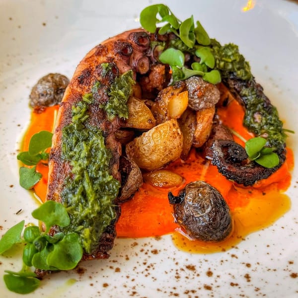 Grilled octopus with pesto, roasted potatoes, and a red sauce on a white plate.